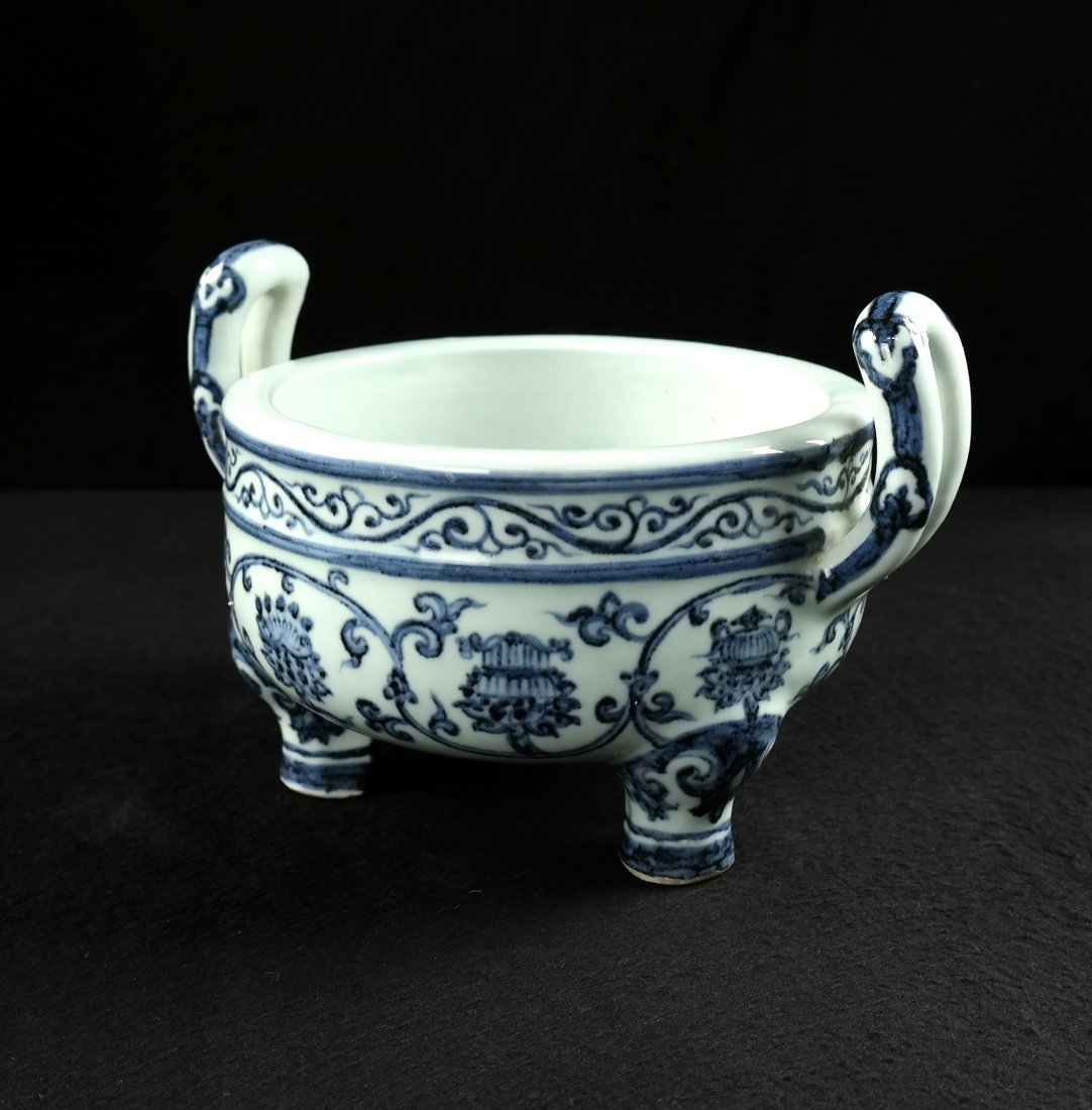Chinese Blue and White Buddhist Bowl: Tripod bowl with attenuated handles at either side. Features all-over scrolling tendril and flower blossom decor. Bears four character calligraphic mark on bottom. [9 3/8" W x 7 1/4" D x 6 1/8" H]. In