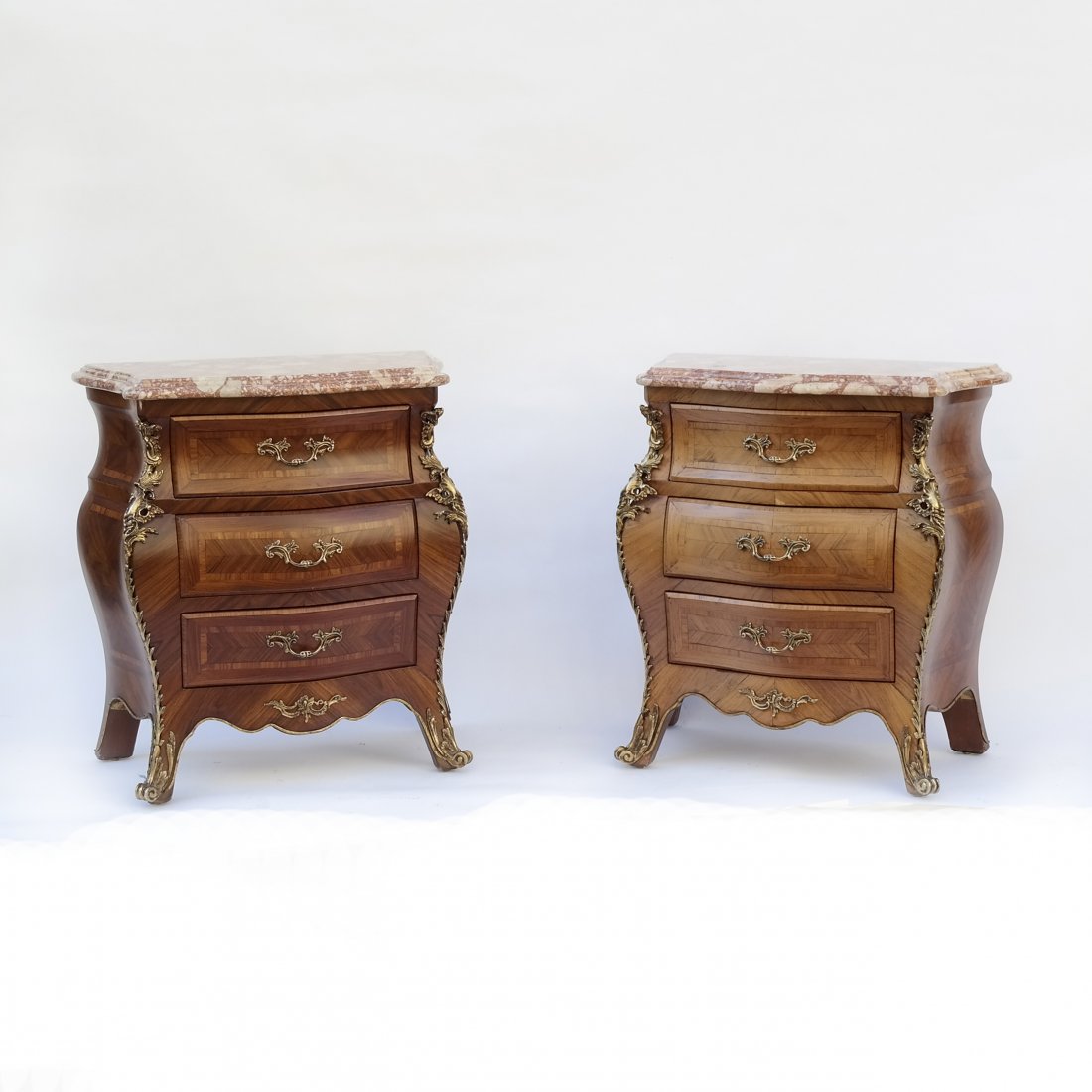 Two Louis XV-Style Bombe Nightstands: Each with ormolu mounts and three drawers. Each stand bears different finish. [23" W x 12" D x 26" H].