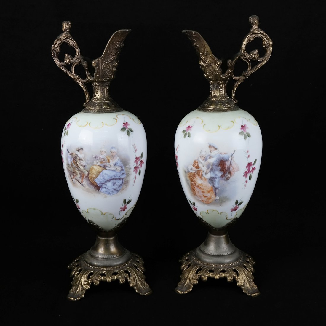 Pair of Continental Gilt Metal Ewers: Pair of Continental gilt metal-mounted opaline glass ewers, each printed with a courting scene amid floral sprays. [7" W x 17 1/2" H]. Both exhibit surface wear.