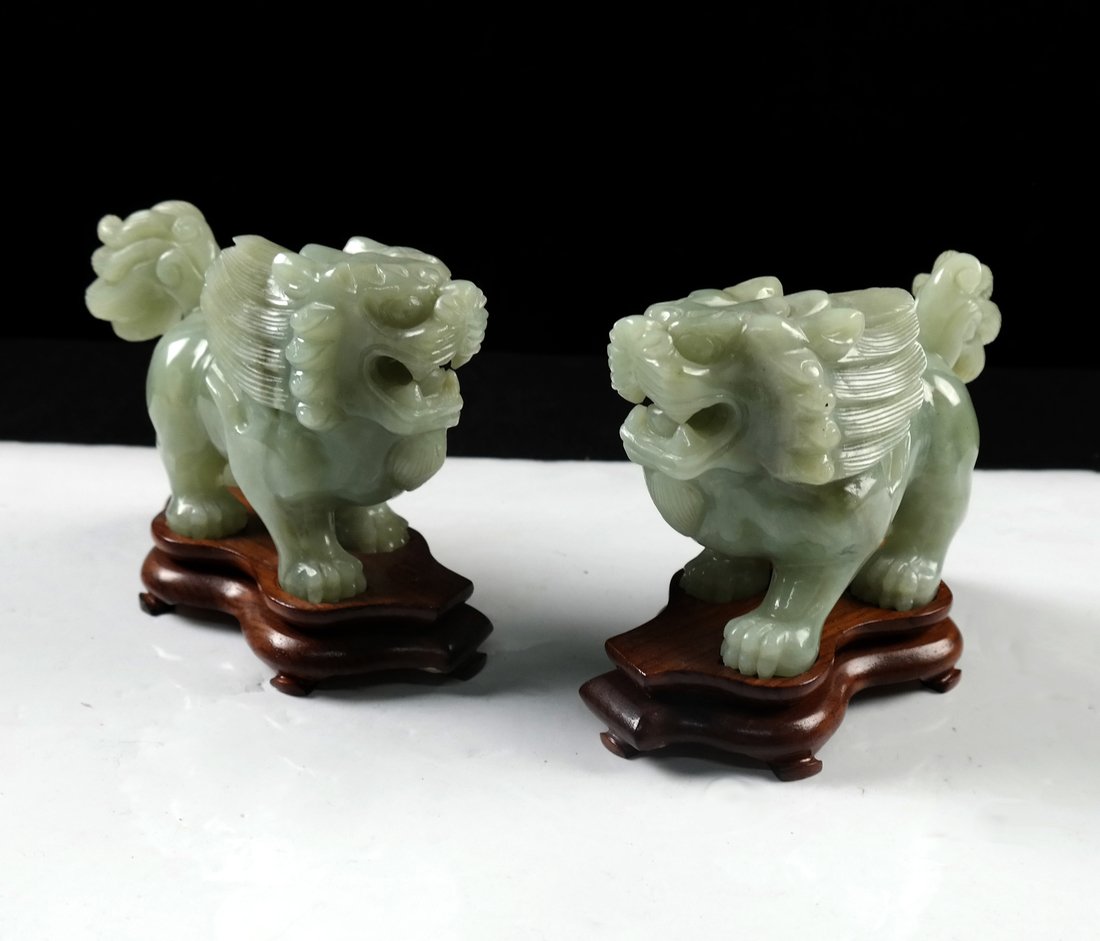 Pair of Chinese Hardstone Lions: Each modeled in jade green stone with stylized manes and tails. With conforming wood bases. [5 3/4" W x 2 1/4" D x 3 1/2" H; 4 1/2" H with stand]. In good condition.