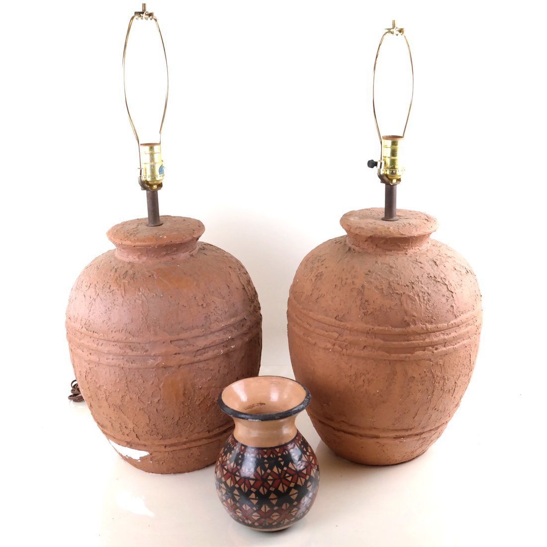 3 Pre-Columbian Style Decorative Objects: One pair of faux terracotta lamps. [26 1/2" H x 11 1/2" Dia]. Paint splatter. Flared rim vase [7" H x 6 1/2" Dia]. Chips and paint loss.