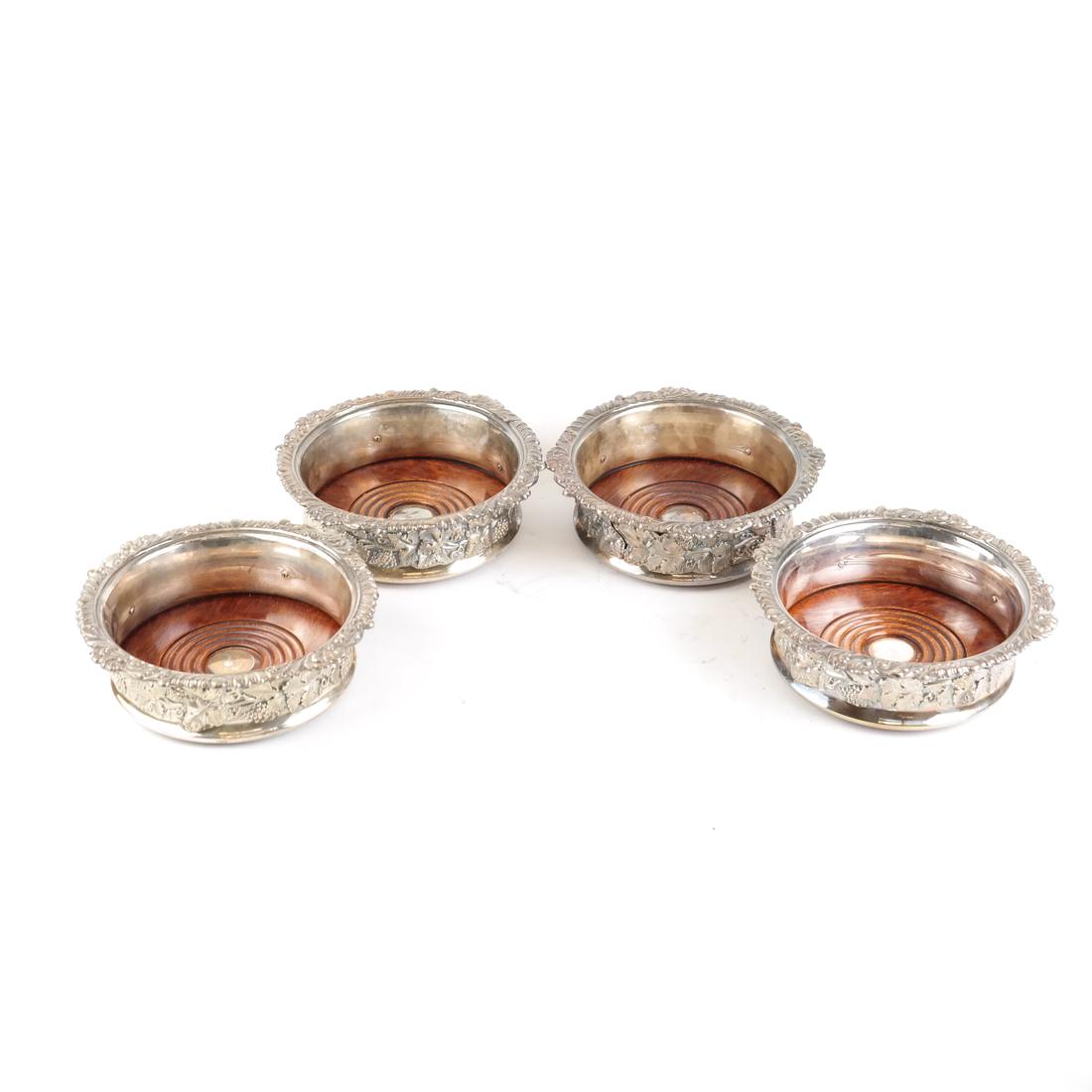 Four Silver Plate Wine Coasters: Four silver plate wine coasters with wood inserts and decorated with a grape and vine motif. [2 1/4" H x 6 3/4" Dia]. Overall good condition with minor wear and scratches.