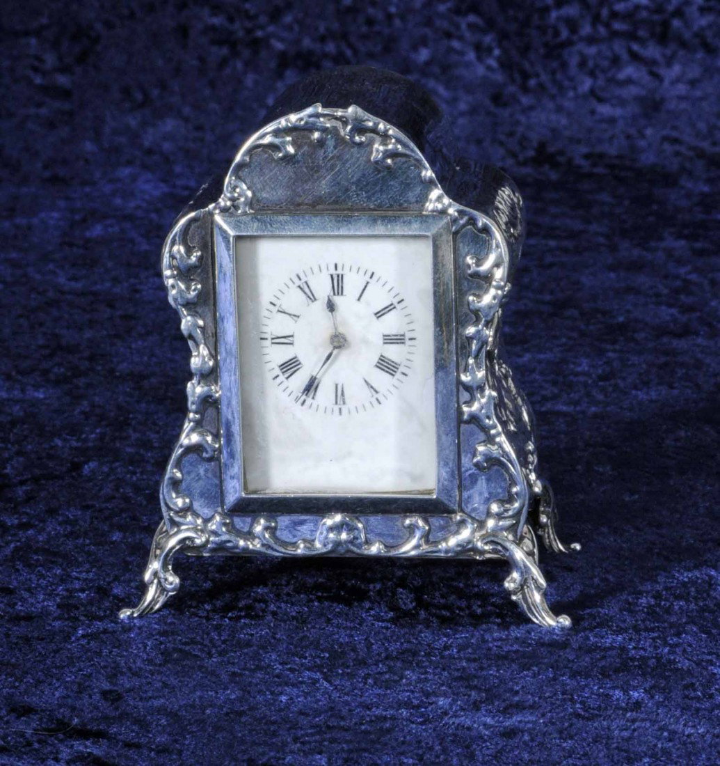ANTIQUE ENGLISH SILVER TRAVELING CARRIAGE CLOCK IN: ANTIQUE ENGLISH SILVER TRAVELING CARRIAGE CLOCK IN THE SHAPE OF AN FOOTED ARMOIRE. FIGURES IN RELIEF ON THE SIDES. FLORAL SCROLL DESIGN FRONT, RESTING ON FLORAL DESIGN FEET. FRENCH MOVEMENT. 3 3/4" H 