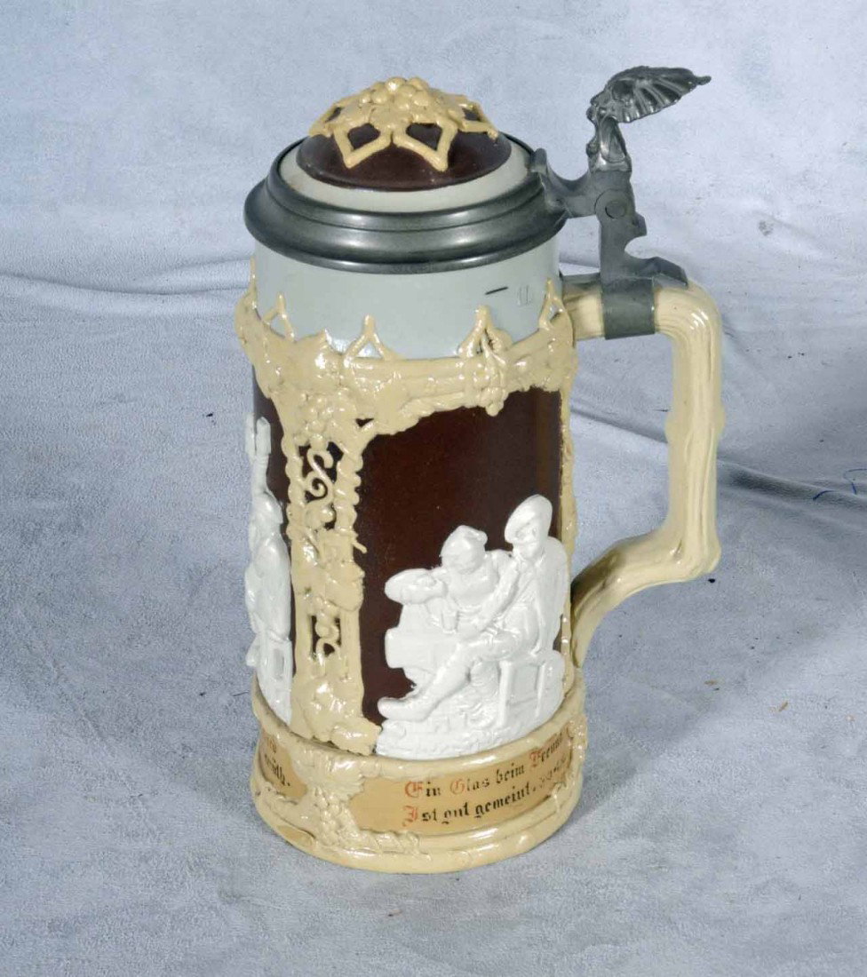 GERMAN CERAMIC METTLACH BEER STEIN W/ A BROWN BACK: GERMAN CERAMIC METTLACH BEER STEIN W/ A BROWN BACKGROUND AND PANELS OF WHITE FIGURES IN RELIEF. CREAM COLOR VINE DECORATION. MAKER, VILLEROY & BOCH 1 L. 9 1/2" H X 5 3/4" W.