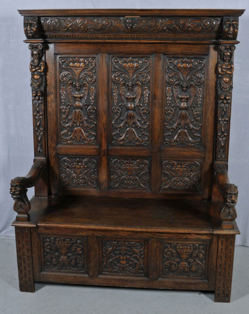 ANTIQUE ENGLISH OAK HALL BENCH. HEAVILY CARVED PAN: ANTIQUE ENGLISH OAK HALL BENCH. HEAVILY CARVED PANELS W/ FIGURAL AND FLORAL RELIEF DECORATION. FIGURE OF A HEAD AT THE TOP, FIGURES ON THE SIDES & CARVED ARM RESTS. LIFT UP BENCH. 68 1/4" H X 54" W. (