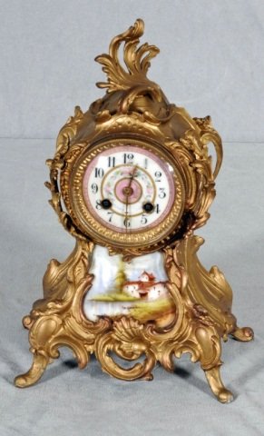 GILT ORMOLU MANTEL CLOCK. PORCELAIN FACE & PORCEL: GILT ORMOLU MANTEL CLOCK. PORCELAIN FACE & PORCELAIN LANDSCAPE DECORATION ON THE BOTTOM. CLOCK NOT WORKING. 13 1/2" H X 9" W.