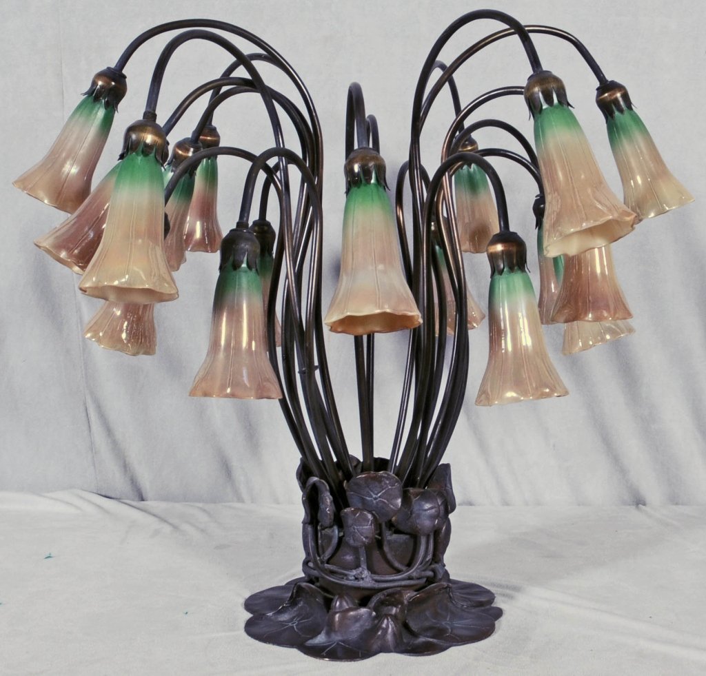 TIFFANY STYLE 18 LIGHT LILLY TABLE LAMP. BRONZE BASE. L: TIFFANY STYLE 18 LIGHT LILLY TABLE LAMP. BRONZE BASE. LILLY GLASS SHAPED SHADES. GREEN TO BROWN. GOOD. 21 3/4" H X 25' DIA. FROM THE SANTA MONICA CONDOMINIUM OF LARRY HAGMAN, STAR OF "DALLAS" AND "I D