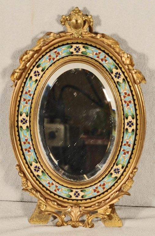 FRENCH BRONZE AND CHAMPLEVE OVAL TABLE MIRROR. MULTI: FRENCH BRONZE AND CHAMPLEVE OVAL TABLE MIRROR. MULTI COLOR FLORAL ENAMEL BORDER. BEVELLED MIRROR. SCROLLED LEAF FRAME. GOOD. 9 1/4" H X 5 3/4" W.