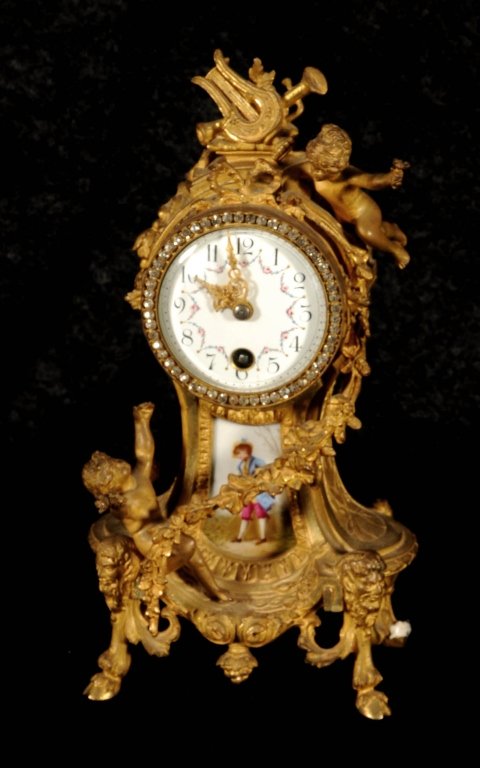 FRENCH GILT ORMOLU MANTLE CLOCK. LOUIS XV STYLE. THE: FRENCH GILT ORMOLU MANTLE CLOCK. LOUIS XV STYLE. THE CASE HAS MUSICAL INSTURMENTS, CUPIDS, AND FLORAL SWAGS. ENAMEL FACE AND A PAINTED PORCELAIN PLACQUE OF GENTLEMAN. CLOCK NOT WORKING. 10 1/2" H X 5 