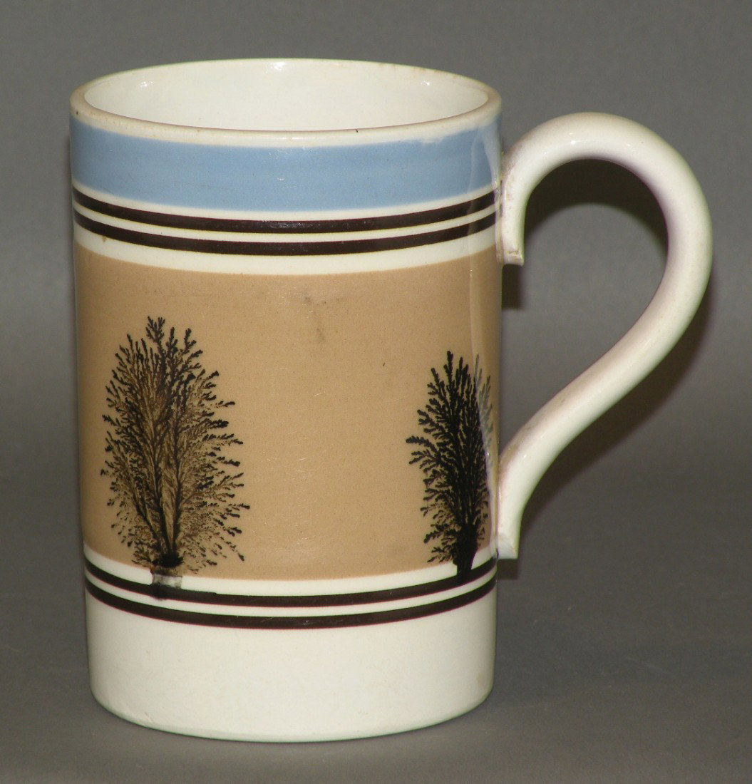 Mocha handled mug: ca. 1860; with ironstone body, black seaweed on tan band bracketed by 2 black bands & surmounted by a blue bank, 3 ½"d, 5 1/8"h;