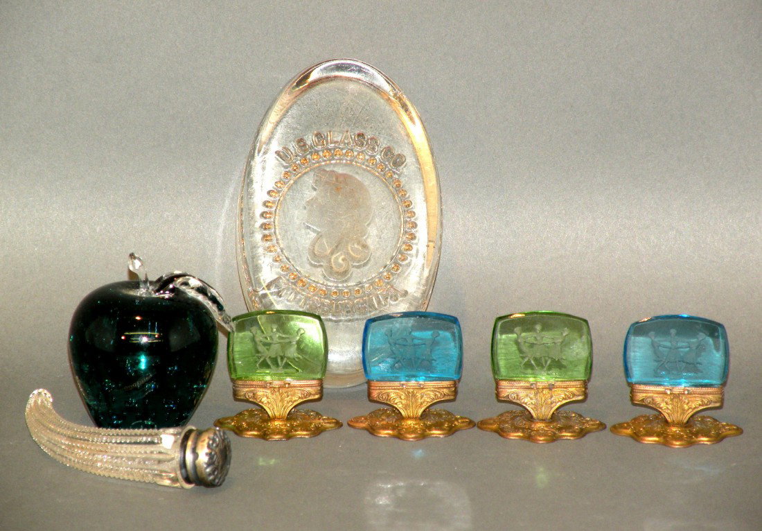 7 pieces of glassware: ca. 1900-30; colorless oval molded glass paperweight marked "US Glass Co. Pittsburgh, PA" encircling a woman's head, 1"x 2 5/8"x 4 ¼"; signed "Pairpoint" teal green bubbled glass apple form paperweig