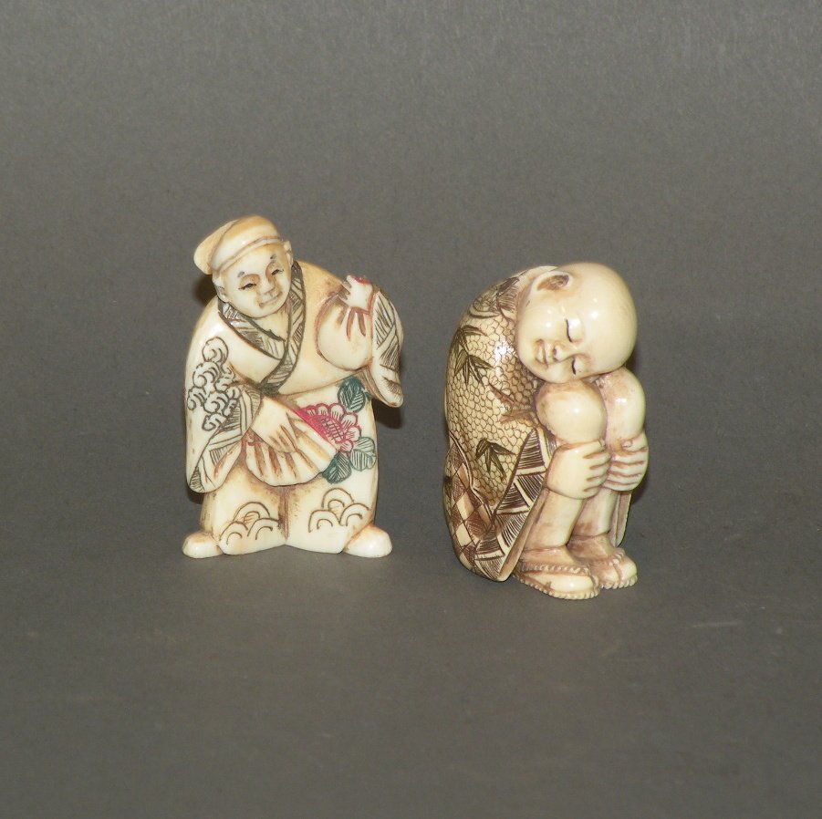 2 carved ivory Japanese netsukes: ca. 1880-1930; sleeping huddled child with black and rose stained design signed on base, 1 ¾”x 1”x 1 1/8”; standing woman holding fan and sack with black, green and rose stained design signed o