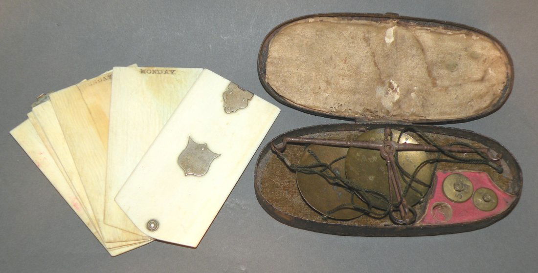 2 traveler’s accessories: ca. 1800-1900; tin cased hanging scales with brass trays and 2 weights; 1850’s era gentleman’s ivory pocket weekly calendar made of thinly sliced ivory for each week day with 2 out books having ni