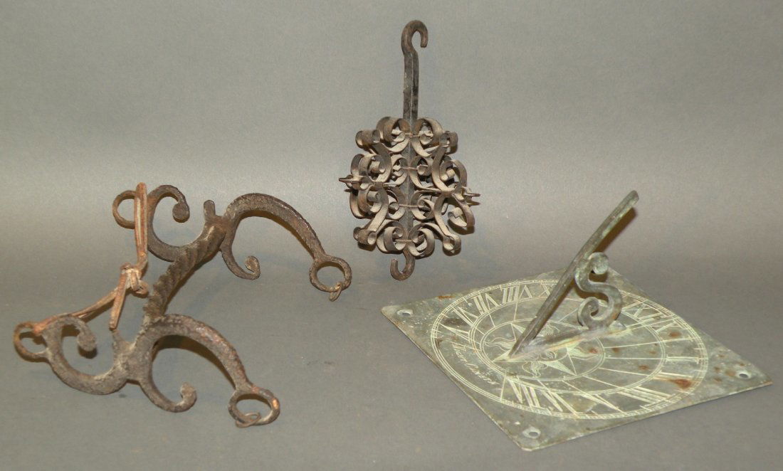 3 primitive items: ca. 1750-1950; brass sun dial finely engraved with a sun face, 6 1/8”x 6 1/8”x 3 ¼”; early horse bit with scrolled ends and a twisted shaft, 6”x 6 1/8”x 2 ¼”; late scroll work hanger, 3
