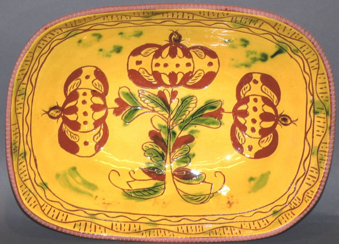 Breininger sgraffito redware loaf dish: ca. 1972; foliage and three pomegranates design having yellow overcoat with green sponging and incised “Robesonia, PA, 1972, L&B Breininger” on bottom, 3”x 10 ¼”x 13 ¾”;