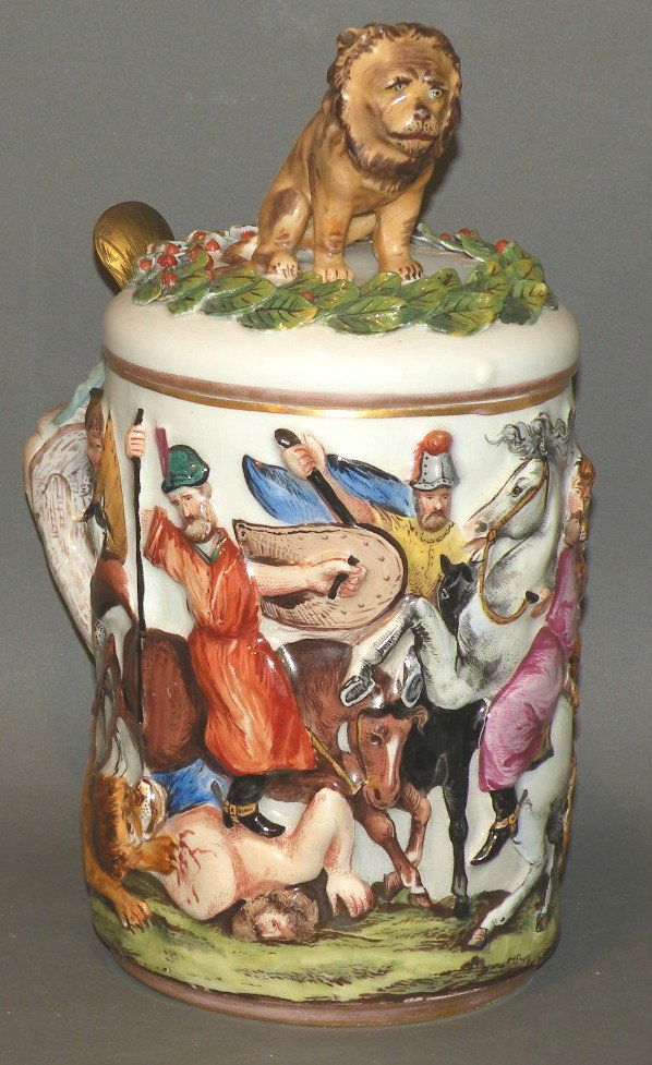 Capodimonte style stein: ca. 1920; molded lion encircled by molded leaf and berries on hinged lid with the body in bas-relief depicting a battle scene with manufactures mark on base, 4 7/8”d, 11”h;