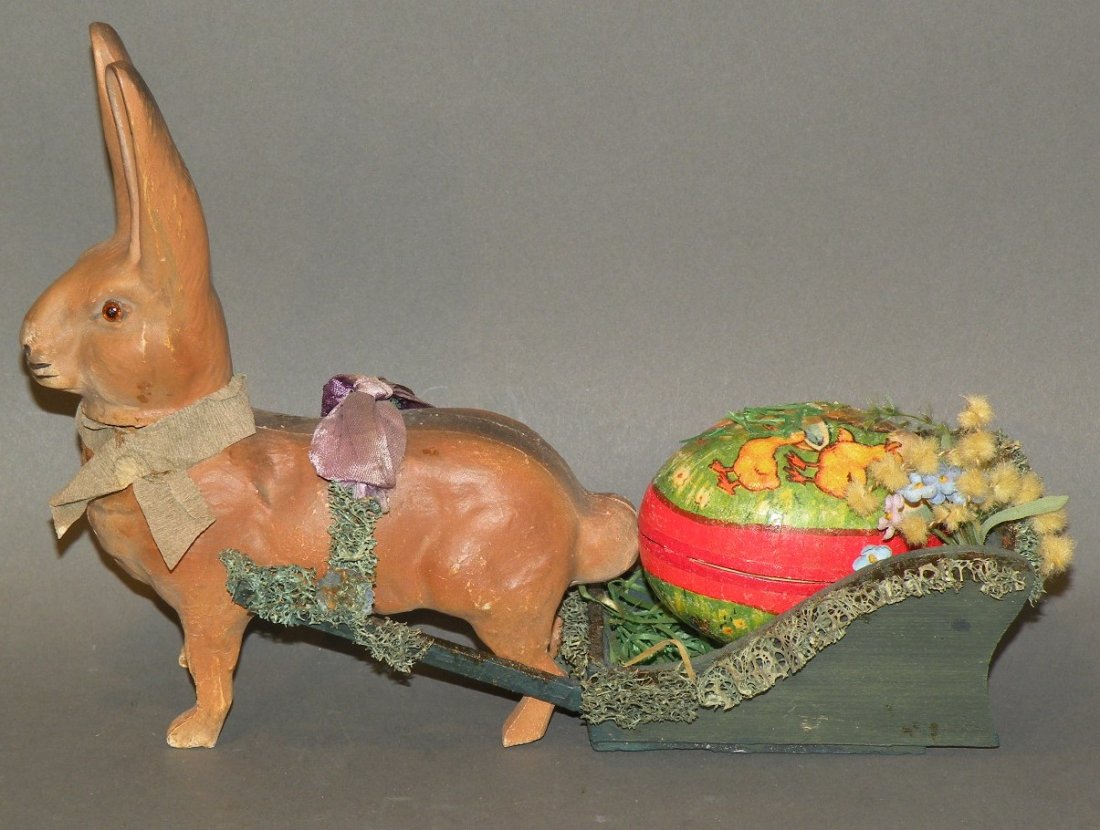 Rabbit candy container: ca. 1910-20; glass eyed rabbit candy container pulling a sled with a papier mache egg and two cotton batting chicks, 9”;