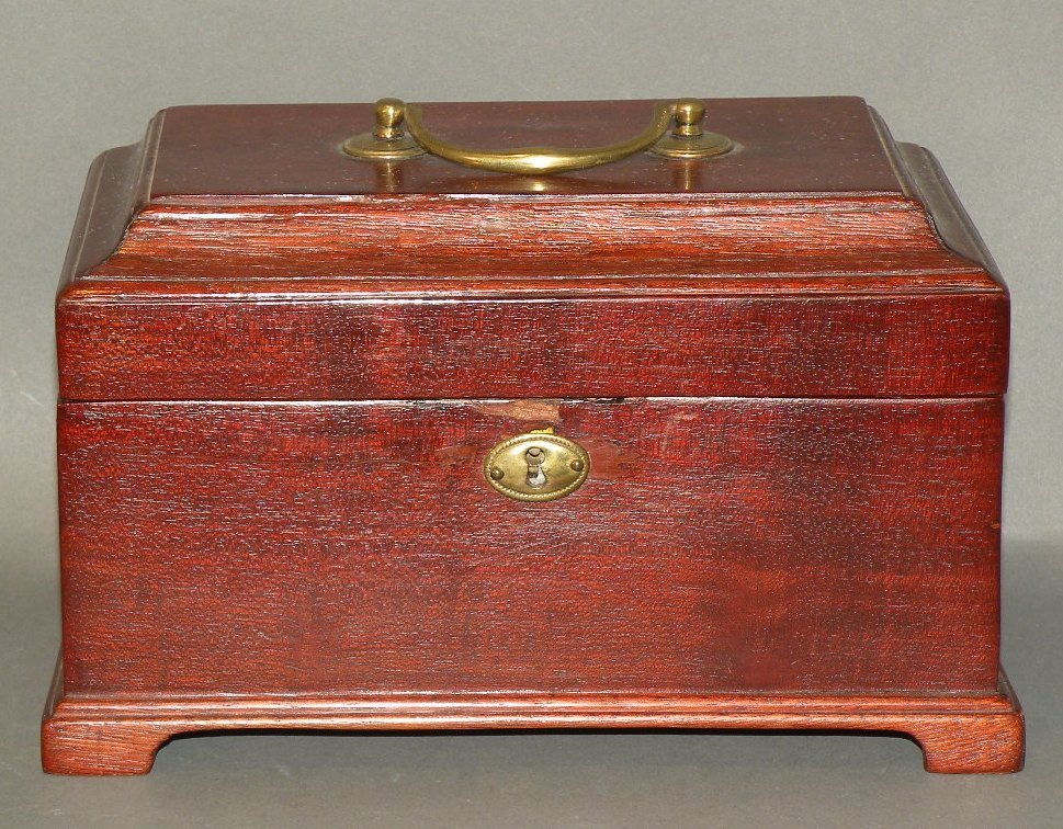 Mahogany tea caddy: ca. 1800-50; with a molded lid, bracket base, brass bale handle and escutcheon and interior fitted with three tin canisters, 8 7/8”x 5 3/8”x 5 ½”;