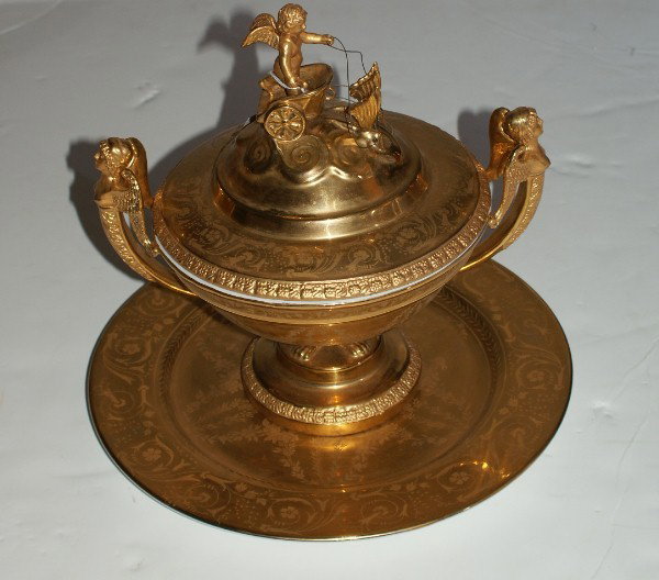 French Empire Sevres gilt porcelain centerpiece: French Empire Sevres gilt porcelain centerpiece bowl and underplate; the bowl decorated with Cupid riding in a chariot with winged caryatid handles on paw feet and circular foot on a circular tray. H: