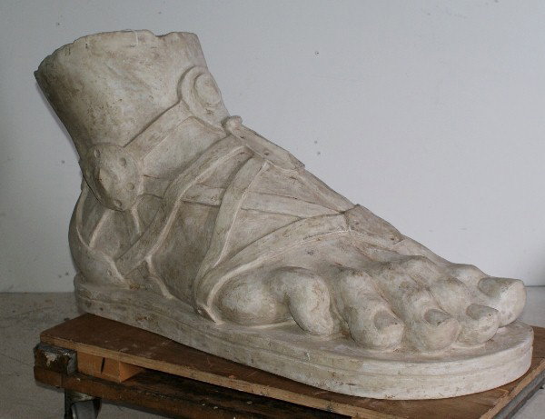 Stone Roman sandal with a thin thong, right. H: 2: Stone Roman sandal with a thin thong, right. H: 21" W: 33" D: 15"