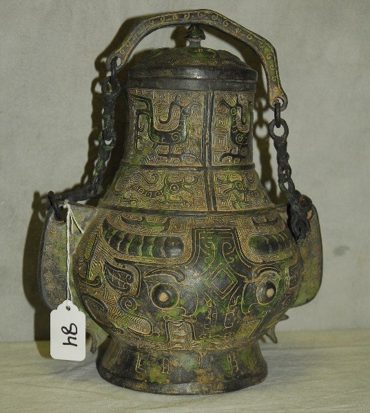 Antique Chinese bronzed vessel with cover ornately cast: Antique Chinese bronzed vessel with cover ornately cast with animal and caligraphy design on a raised foot and with a hanging chain. H:11"