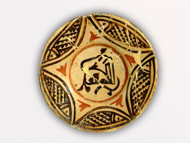 AN NISHAPUR CERAMIC PLAT EASTERN IRAN, 10TH CENTURY: A Nishapur Plat , With flat outturned rim, the interior painted in green, yellow and manganese with split and incised decoration , corners designed paint fish interior painted with red flowers . Meaur
