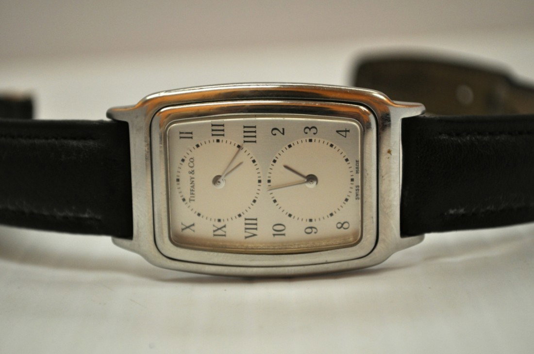 TIFFANY & CO DUAL TIME ZONE WATCH: TIFFANY & CO DUAL TIME ZONE WATCH IN STAINLESS STEEL WITH LEATHER BAND, Case measures 26mm x 43mm and when closed--crowns are enclosed and requires opening the hinged case to set separate time zones. 
