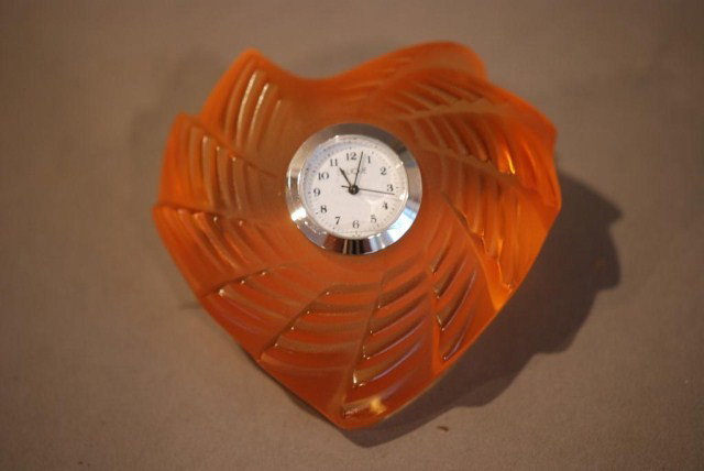 LALIQUE SAINT-VALENTIN CLOCK: Burnt orange color crystal with inset clock, new in box with papers, signed Lalique France with an R in a circle, 1 1/2"h x 3 1/4"w x 3"d. In good condition.