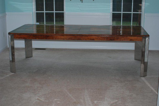 MILO BAUGHMAN DESIGN DINING ROOM TABLE: Burl walnut veneer with a highly polished finish, supported by chrome legs and 2-extra leaves in a fitted case, 29 1/2"H X 44"W X 96"L with 2-18" leaves, opens to 132". In good condition.
