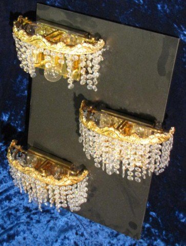 3-MODERN HOLLYWOOD REGENCY FIXTURES: Electrified brass sconces with dripping crystals, mounted on a display board of approximately 14" X 22", Light signs of dust and wear, some crystals are missing, 9" X 7" X 4"D.
