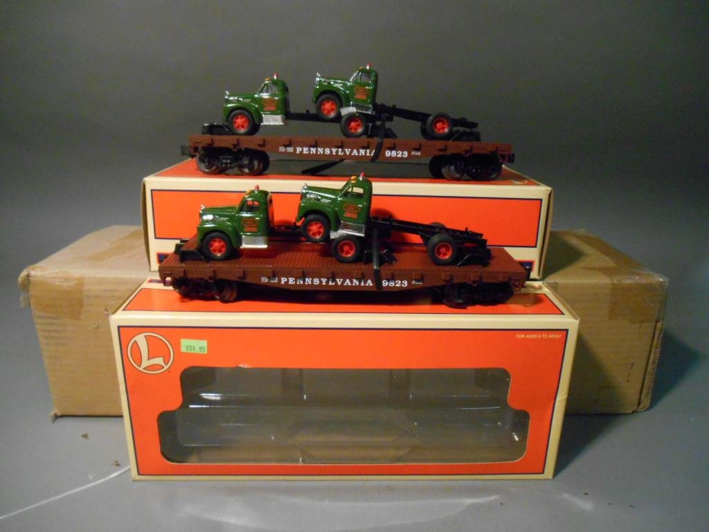 Lionel Flatcars with Trucks: Lot of two Lionel modern era O gauge #17518 PRR standard O flatcars with two Corgi Mack trucks. Both come with their original boxes.