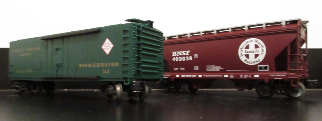 Lionel O Gauge Freight Cars: Two (2) Lionel Modern Era O gauge freight cars. There is an REA scale reefer and a BNSF scale covered hopper car. Excellent condition.