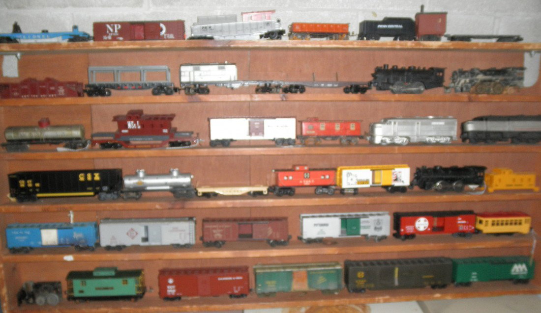 SHELF OF O GAUGE TRAINS: Third from the top shelf of O gauge trains, including 2 nonpowered Alco diesel engines and 6 freight cars (a couple incomplete).