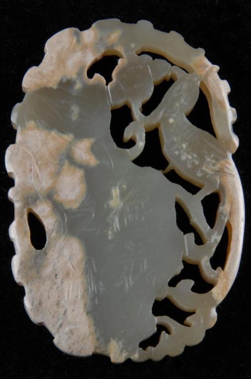 A CHINESE MOTTLED JADE RETICULATED PLAQUE: of oval form and depicting a bird amongst scrolling foliage and blossoming prunus reversing to a bird above stylized rockwork with four character mark inscription within a shaped border. Height: 2 1/2