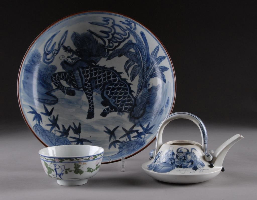 THREE CHINESE AND JAPANESE PORCELAIN WARES,: LATE 19TH EARLY 20TH CENTURY, comprising a Japanese blue and white teapot decorated with smiling Buddhist and Taoist deities and auspicious symbols beneath an arched handle above a rectangular spout c