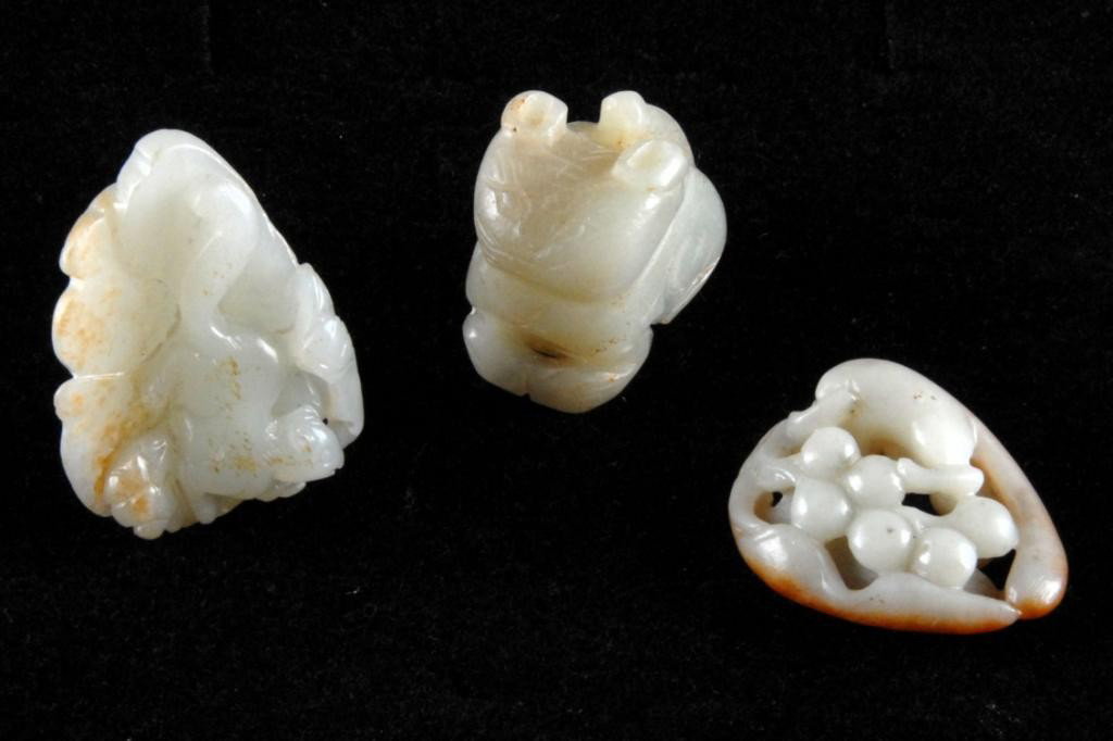 A GROUP OF THREE CHINESE CARVED JADE PENDANTS,: one detailed in celadon green jade modeled as a cat with stylized stars, height: 1 1/4"; a white and russet brown included pendant of a squirrel foraging in a grape cluster, length: 1 5/8"; a celadon 