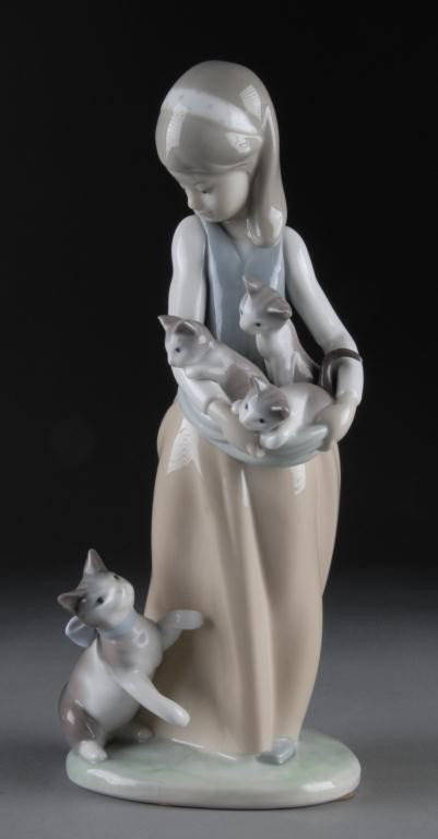 A LLADRO FIGURINE FOLLOWING HER CATS #1309, 1974: The figure with a hair scarf, blue vest, and beige skirts carrying three gray and white kittens in a apron, a cat playing at her feet, on a conforming grass-green base, with blue bellflower Lladro bac