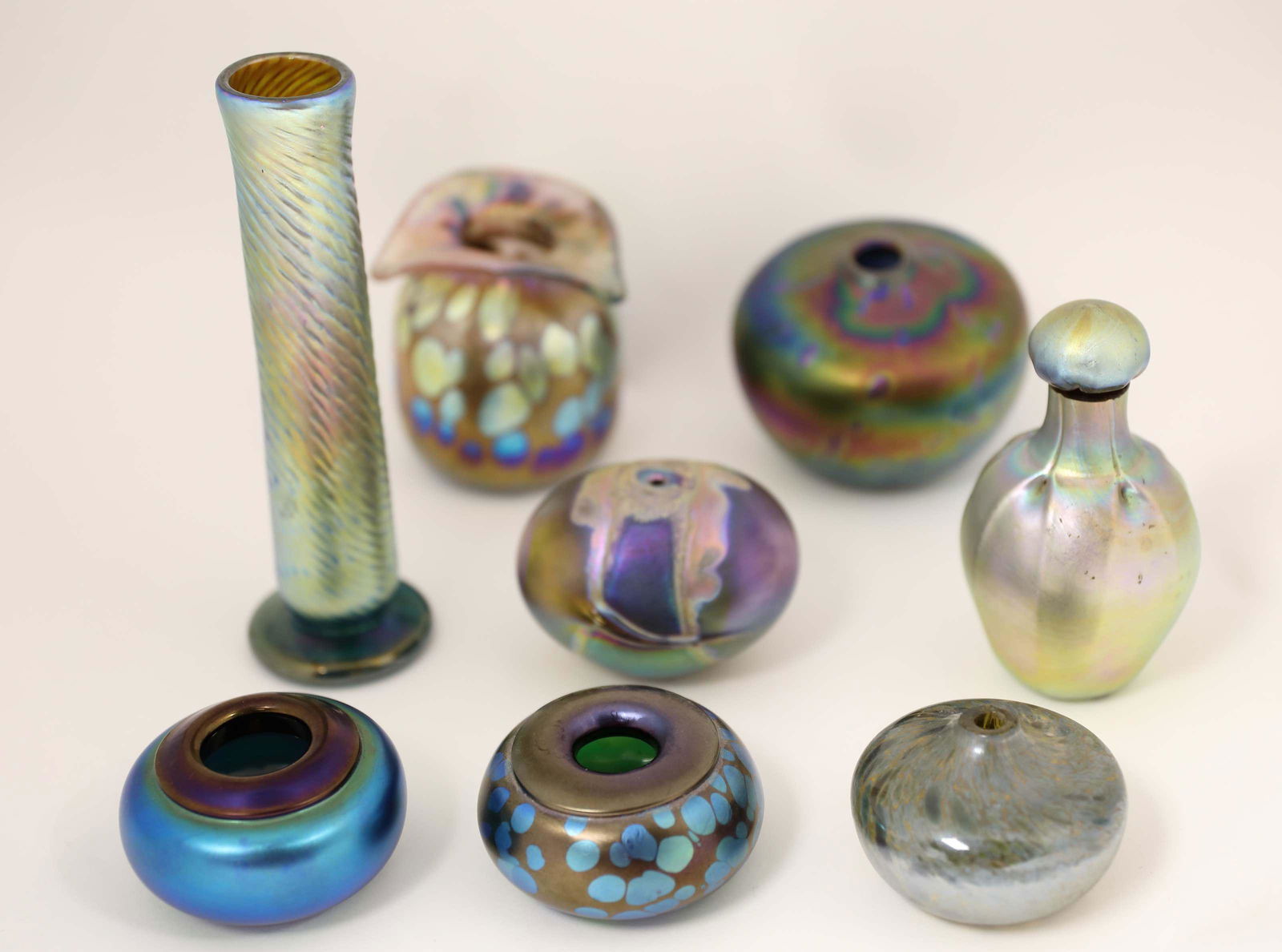 (8) Irridesant Vases 2-Orient & Flume 1-John Cook: (8) Irridesant art glass vases (2) Orient & Flume small paint pots. (1)John Cook Phoenix glass bottle stopper repaired. (1) Signed tall bud vase. (4) Unmarked vessels. Measure 1.75" to 8" tall.
