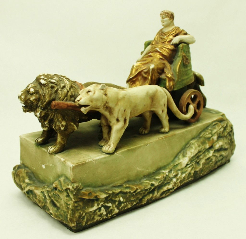 Imperial Amphora Porcelain Sculpture: Imperial Amphora (Austria) porcelain sculpture depicting a roman emperor in a chariot pulled by lions. Base has been repaired, lion's tail missing. Dimensions: 14" x 11" x 6 1/2" Style/Time Period: