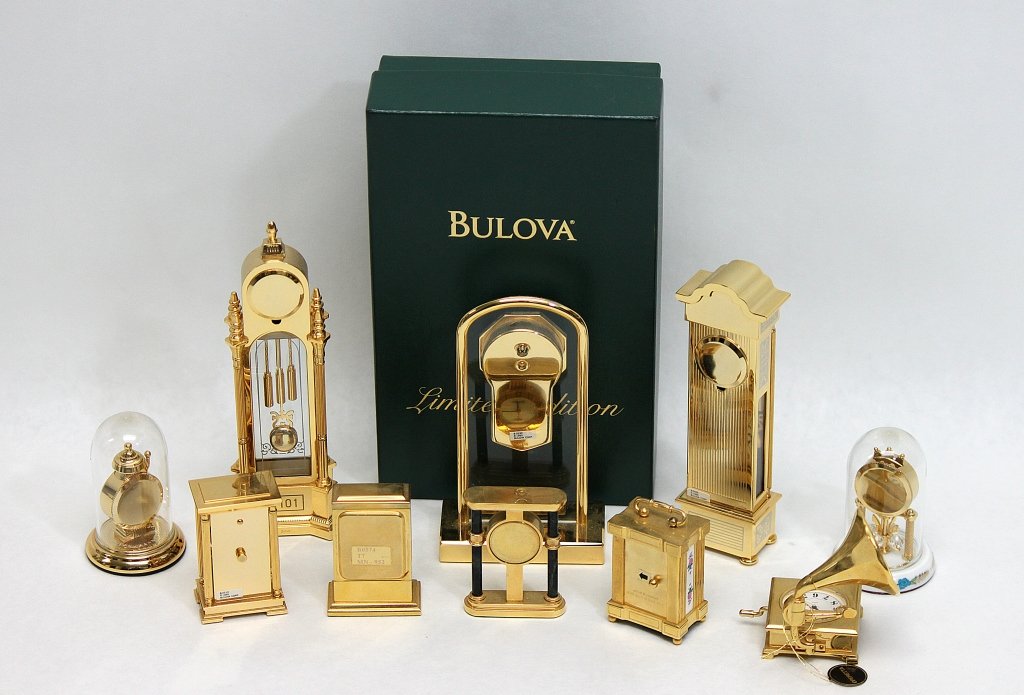 (10) Bulova Miniature Clocks: Lot of ten Bulova miniature clocks: two grandfather clocks, one wall clock on a glass base, three anniversary clocks, a mantle clock, a carriage clock, and two novelty clocks, one with a victrola and