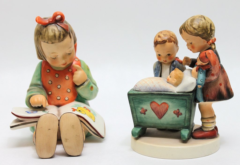 (2) Goebel German Porcelain Figurines: Two Goebel German porcelain figurines; one of a girl with a picture book, the other of two children with an infant in a cradle. Girl with book measures 4 x 4.75" x 5.5", the two children measure 4.5" 