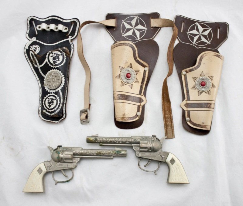Lot Of 2 Young Buffalo Bill Cap Guns w/ 3 Holsters: Lot of two Young Buffalo Bill cap guns with matching holsters and one additional holster. Both guns in working condition with some wear from use. One holster has original belt. Guns Measure 7" x 1" Ho
