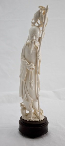 Ivory Carving Of Confucius w/ Fishing Pole: Hand carved ivory figural of Confucius holding pipe in one hand and fishing pole in the other. Wearing traditional robe tied with a bow. At his feet is fishing basket and plant. Raised on hand carved