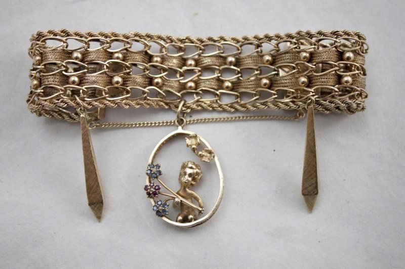 14k Gold Bracelet w/ Hanging Charms: 14k Gold bracelet with three hanging charms. Center charm has cherub holding 3 flowers accented with gemstone pedals. On either side hang obelisk charms. Features box clasp with safety chain. Marked 1