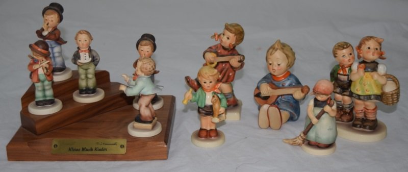 10 Goebel M.J. Hummel Musical Figurines w Stand: 10 Goebel West Germany M. J. Hummel musical figurines of children caroling and playing musical instruments. Included is a wooden stand with a brass plaque titled "Kleine Musik Kinder". 7 Figures are 3