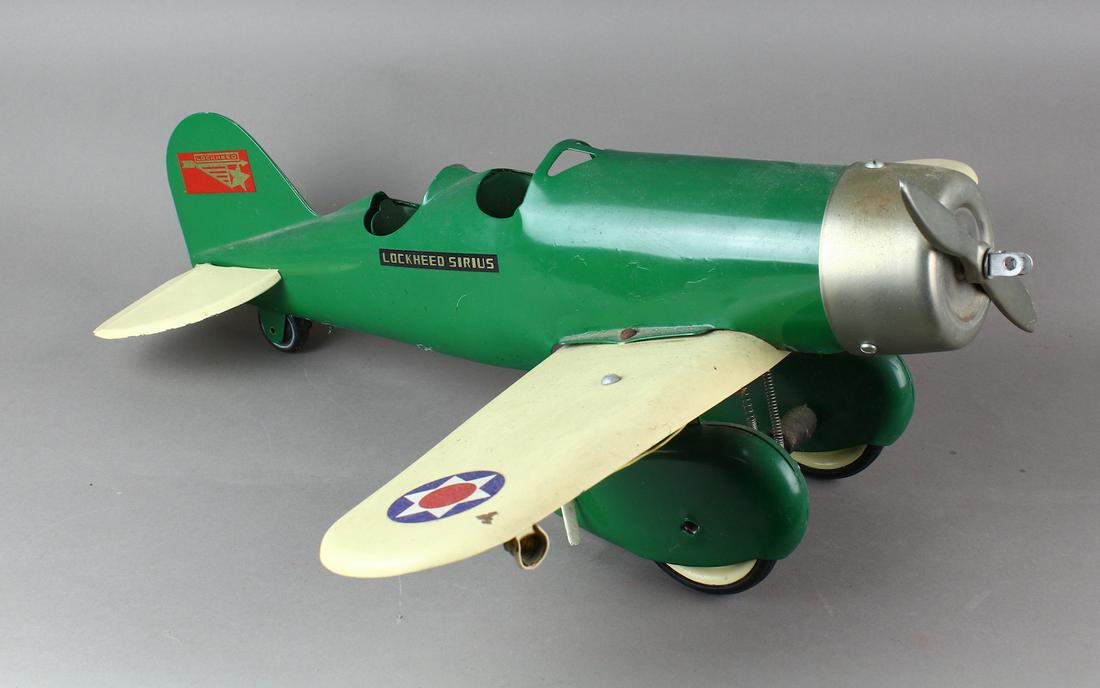 1930s Steelcraft Lockheed Sirius Airplane: 1930s Steelcraft Lockheed Sirius Airplane. Pressed steel, fuselage done in green, double cockpit, white wings and tail wing, decals on fuselage and white tailfin, full wheel covers, single prop, nicke