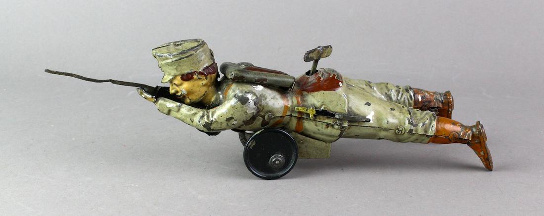 German Tin Prussian Crawling Soldier With Gun: Very scarce c.1915 German wind up soldier with gun, possibly Gunthermann. Off center wheels simulate crawling motion to move soldier low on the ground to shoot. Hand painted 11 inches long, one shoe s