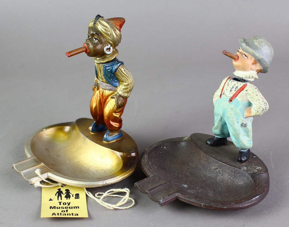 Pair of Austrian Cold Painted Cigar Smoking Boys Ashtray Nodders: Austrian Cold Painted Cigar Smoking Boy Ashtrays. Metal with bright color painted boys smoking cigars. Heads bob. Label from Atlanta Toy Museum on the African American smoker.