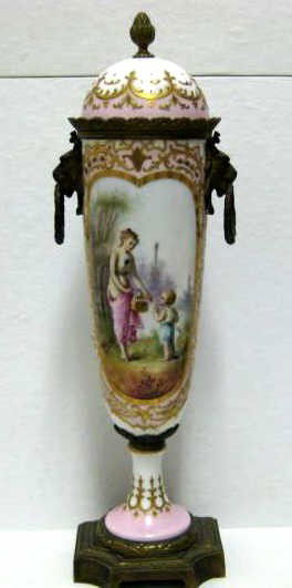 SEVRES STYLE PORCELAIN LIDDED URN: Gilt brass mounted, footed U-shaped, painted two reserves of a Classical garden scene with figures and floral bouquet, signed 'Roche', early 20th century. Height 14 3/4 in.