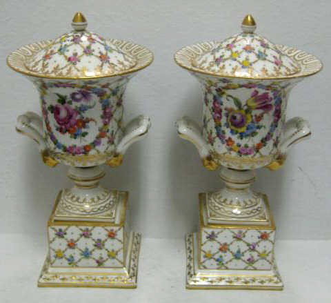 PAIR OF GERMAN PORCELAIN LIDDED URNS: Carl Thieme and VEB Saxonian Porcelain, Potschappel, early 20th century. Each footed urn with two handles mounted to a square pedestal decorated in French style of painted floral trellis and floral me